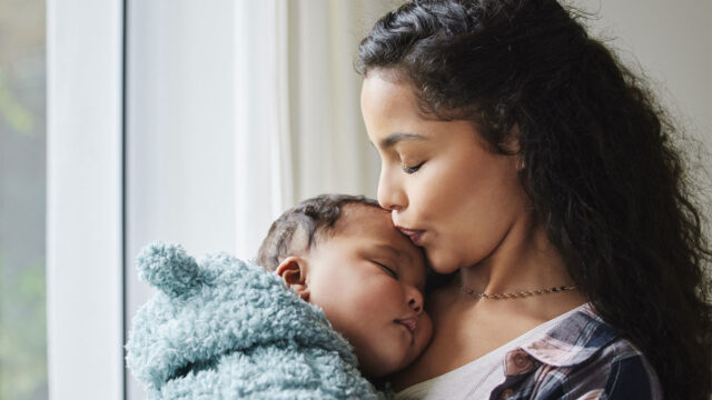 Photo of a young mother giving her baby a kiss at home